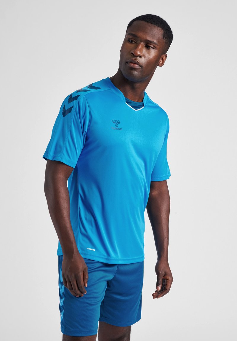 Camiseta atlética azul hecha de material ligero, con mangas cortas, un escote en V y acentos negros en los hombros. Usada con pantalones cortos a juego.
