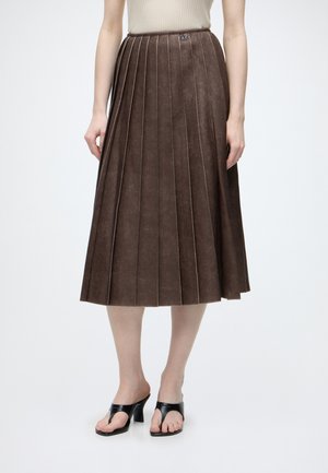 Gonna midi plissettata marrone indossata con sandali neri con tacco e top beige senza maniche, mostrata dalla metà del busto ai piedi su sfondo bianco.