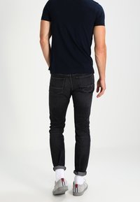 Jeans en denim foncé avec une coupe slim et des poignets retroussés, assortis à des baskets grises et des chaussettes blanches avec une rayure colorée.