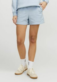 Shorts en coton bleu clair avec une taille élastique, des poches latérales et une coupe décontractée, associés à des chaussettes blanches et des baskets beiges.