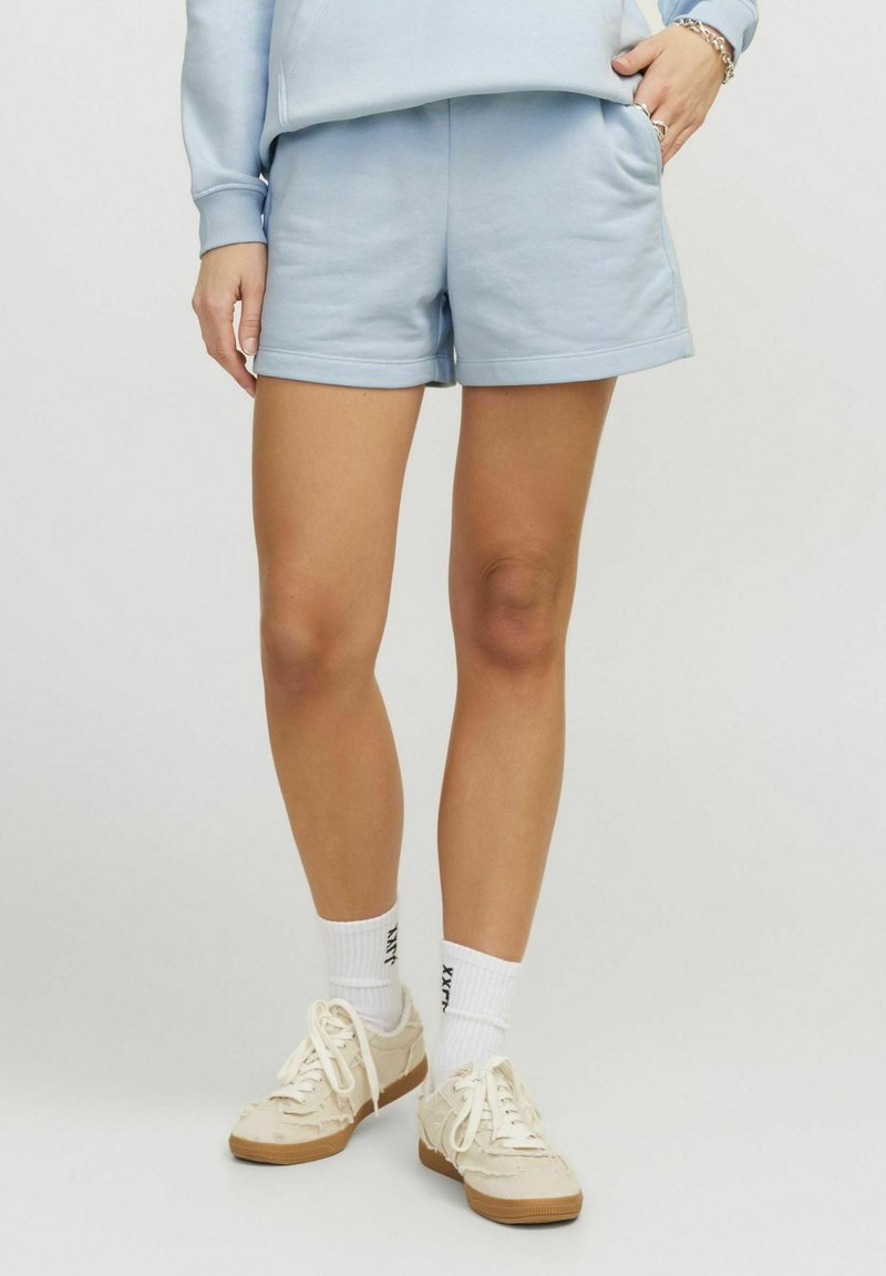 Shorts en coton bleu clair avec une taille élastique, des poches latérales et une coupe décontractée, associés à des chaussettes blanches et des baskets beiges.