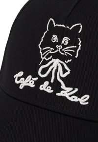 Căciulă neagră cu textură în carouri, având un design brodat alb cu pisica și textul "Café de Kal" scris cu font cursiv.