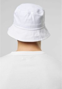 White cotton bucket hat with a rounded crown and wide, downward-sloping brim. Features a stitched band just above the brim.