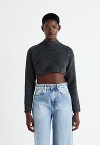 Pulover tricotat de culoare gri închis, cu mâneci lungi, guler înalt și textură moale, purtat cu blugi din denim ușor albastri, cu talie înaltă.