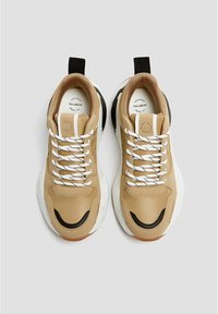 Chaussures de sport beiges avec des lacets blancs, des accents noirs et une tige texturée. Semelle rembourrée et languette à l'arrière pour faciliter l'enfilage.