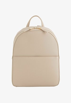 Mochila minimalista beige con parte superior redondeada, bolsillo frontal, cremallera dorada y pequeño asa superior.
