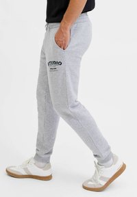 Szare dresy z bocznymi kieszeniami, z czarnym nadrukowanym logo, ściągaczem na kostkach i sznurkiem w pasie. Połączone z białymi sneakersami.