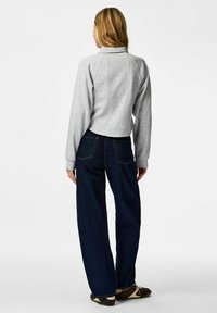 Sweat-shirt court gris avec col et épaules tombantes, associé à un jean large bleu foncé. Tissu doux, lignes épurées, détails minimes.