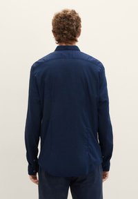 Camicia a maniche lunghe di colore navy, realizzata in tessuto morbido, con colletto classico, polsini con bottone e orlo dritto, dal taglio comodo.