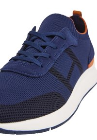 Zapatilla navy con parte superior de malla texturizada, acentos en negro contrastantes y lengüeta en naranja. Presenta cordones planos y una suela de goma blanca.