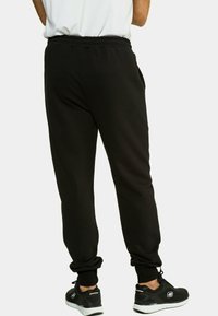 Zwarte sweatpants van zacht materiaal, met een elastische tailleband en taps toelopende boorden. Gepaarde met zwarte sportschoenen.
