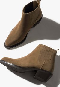 Brown suede ankle boots with a pointed toe, elastic side panels, and a low block heel, featuring a textured black sole and minimal seam detailing.