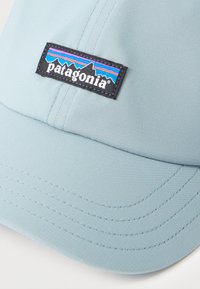 Ανοιχτό μπλε καπέλο με μαύρο ορθογώνιο μπαλώμα λογότυπου Patagonia με σχέδιο βουνού σε μωβ, μπλε και πορτοκαλί ρίγες μπροστά.