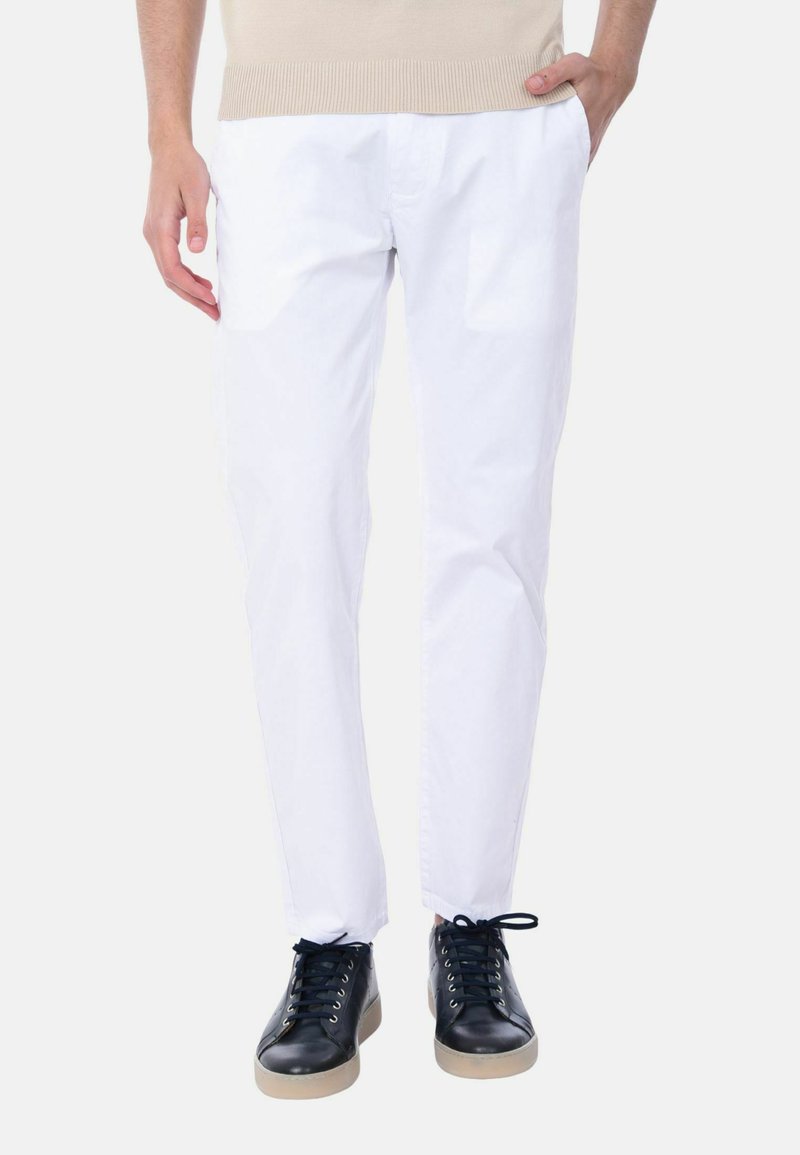 Pantaloni bianchi in cotone con una vestibilità rilassata, abbinati a sneakers in pelle nera con suola in gomma leggera e dettagli con lacci.