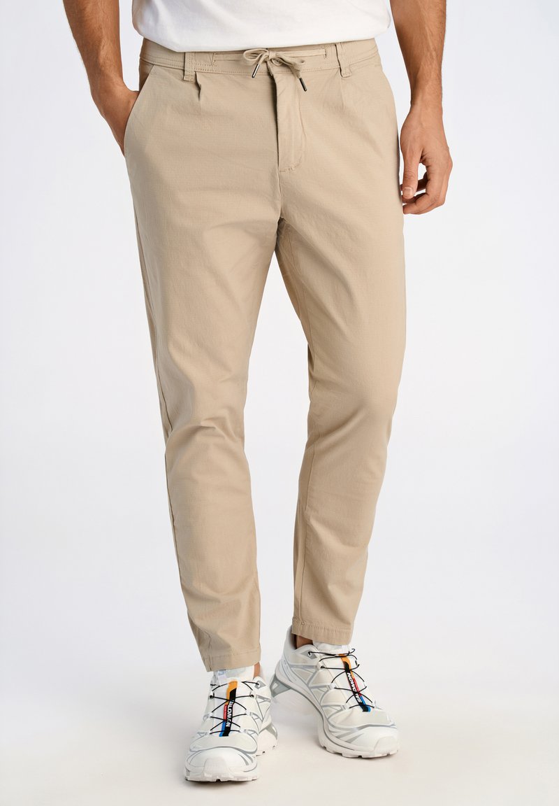 Pantalons beige évasés en tissu léger, dotés d'une taille élastique avec cordon de serrage, de poches latérales et d'une texture lisse.