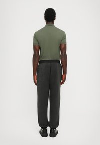 Gray track pants with a tonal pattern, elastic waistband, and cuffed hems, paired with a solid green short-sleeve polo shirt.