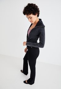 Black denim jacket with a hood, featuring a zip closure and textured pattern; paired with black flared jeans and black flats.