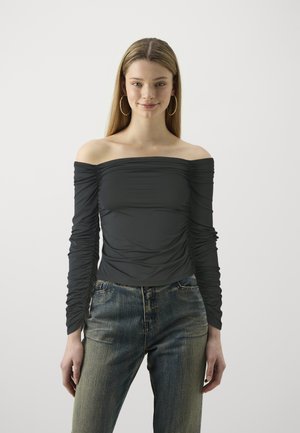Haut gris foncé à épaules dénudées avec de longues manches froncées, associé à un jean taille haute bleu délavé. Aucun motif ou matériel proéminent visible.