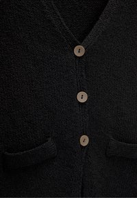 Schwarze Strickjacke mit V-Ausschnitt, beigen Knöpfen und zwei frontalen Taschen aus strukturierter Stoff für zusätzliche Details.