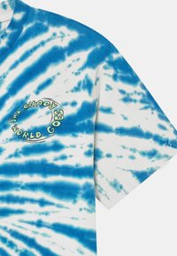 Bavlněné tričko s modro-bílým batikovaným vzorem. Kulatý výstřih s potištěným textem: "SVĚT SE TOČÍ". Krátké rukávy.