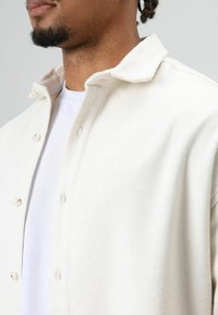 Wit fleece overhemd met knopen, zachte textuur, kraag en zichtbare knopen, gedragen over een wit T-shirt.