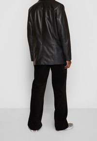 Svart läderjacka med rak skärning, strukturerade axlar och minimala sömnadsdetaljer, tillsammans med svarta kordflorsbyxor och mönstrade sneakers.