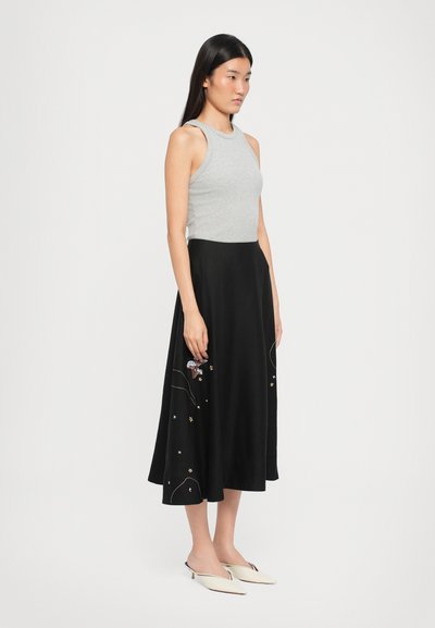 Top gri cu dungi, fără mâneci, combinat cu o fustă neagră în stil A, cu broderii colorate și un design până la genunchi. Pantofi slip-on albaștri completează ținuta.