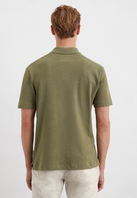 Kurzärmliges, olivgrünes Poloshirt aus einem weichen, strukturierten Stoff. Es hat einen normalen Kragen und seitliche Schlitze am Saum für eine bessere Bewegungsfreiheit.