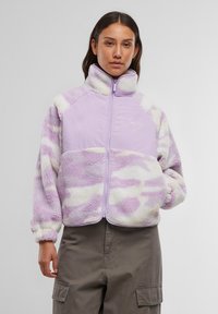 Fialová fleecová bunda so zipsom vpredu, vysokým golierom, obláčkovým vzorom vo svetlejších odtieňoch a elastickými manžetami. Výrazné logo značky na prsiach.
