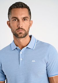 Camisa polo azul claro hecha de tejido texturizado, con un cuello blanco y rayas de acento. Incluye un pequeño logo en el pecho.