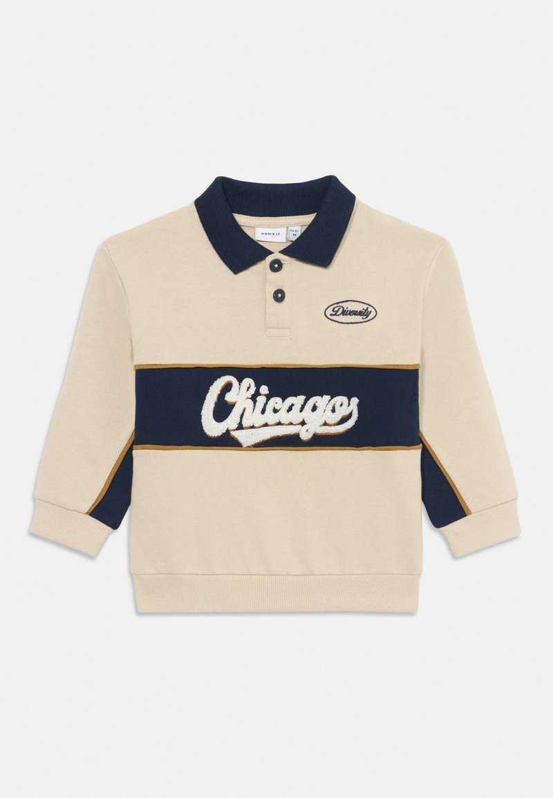 Sudadera tipo polo beige con diseño a rayas en azul marino y blanco. Presenta "Chicago" en texto blanco suave, cuello y puños en azul marino.