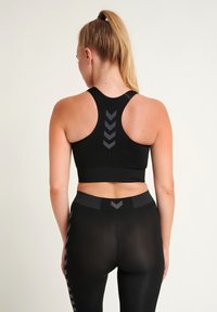 Svart atletisk crop top med racerback-design og grå chevron-mønster; kombinert med høy midje svarte leggings med lignende aksent.
