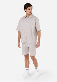 Camicia a maniche corte con bottoni e pantaloni abbinati in beige chiaro con sottili righe verticali, con una tasca sul petto e branding bianco.