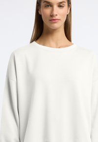Lichtgrijze oversized sweatshirt met een ronde hals en verlaagde schoudernaden, met subtiele textuurdetails bij de kraag.