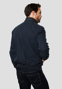 Giubbotto bomber blu navy con orlo e polsini a coste, realizzato in tessuto texturizzato con tasche laterali. Il colletto è leggermente rialzato.