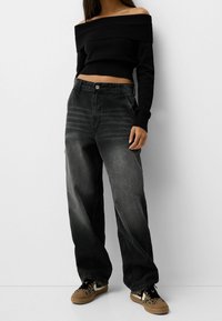 Suéter corto de canalé negro con escote off-the-shoulder, combinado con jeans holgados de color gris oscuro. Las zapatillas cuentan con un diseño de estampado de leopardo.