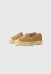 Tan-nahka espadrillit, joissa on juteesta valmistettu espadrilli-pohja. Liukas-malli, jossa on pyöreä kärki ja kohokuvioitu logo etuosassa.