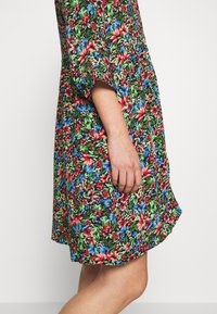 Blommig klänning med svart bakgrund och röda, blå och gröna blommor. Korta ärmar, avslappnad passform och utställd nederkant. Slät tygkvalitet.