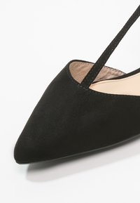 Chaussure plate en suede noir avec un bout pointu, dotée d'une fine bride autour de la cheville et d'un intérieur lisse.