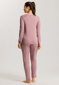 Långärmad, figurnära topp och matchande byxor i mjuk rosa tyg med en slät textur. Enkelt design utan mönster eller detaljer.