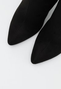 Bottes noires à talons pointus en cuir suede doux. Présente un design épuré avec une texture lisse et une silhouette sans couture.