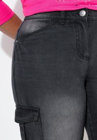 Pantaloni cargo in denim nero con design classico, tasche laterali e una leggera texture sfumata, con dettaglio in metallo argentato alla vita.