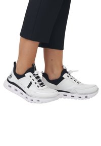 Des chaussures de sport blanches et noires avec une tige texturée, un design à lacets et une semelle rembourrée dotée de sections découpées pour la respirabilité.
