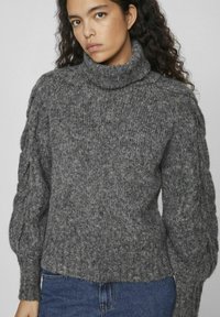 Siv pulli s turtleneck-om, pleten z ribastim vzorcem, z balonastimi rokavi in robom. Združen z modrimi kavbojkami.
