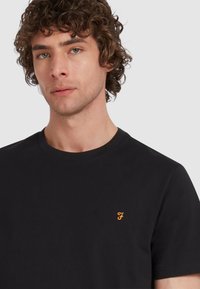 T-shirt in cotone nero con scollo rotondo e maniche corte, dotato di un piccolo logo arancione sul lato sinistro del petto.