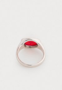 Hõbedane sõrmus, millel on sile ja kaarjas disain ning silmatorkav punane ovaalne kivi, mis on pandud läikivasse raami.