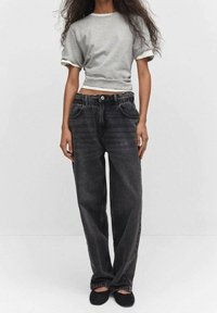 T-shirt grigia accorciata con bordo bianco, abbinata a pantaloni in denim neri larghi con vita elastica e tasche frontali. Calzature nere visibili.