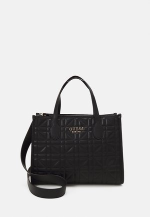 Sac à main Guess en cuir noir matelassé avec deux poignées, une bandoulière amovible, et un logo doré indiquant "GUESS EST 1981" sur le devant.