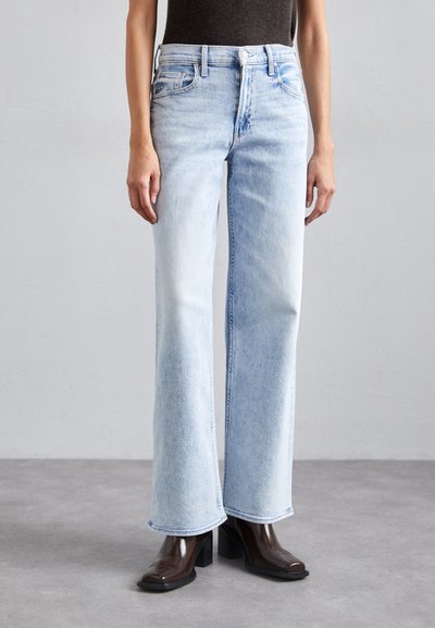 Light-wash denim jeans with wide legs, featuring a high waist, slight distressing, and classic five-pocket design. Paired with brown heeled boots.