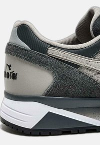 Sneaker con una combinazione di colori grigio e nero, caratterizzata da un materiale testurizzato, accenti in rete e un tallone rinforzato con dettagli del logo visibili.